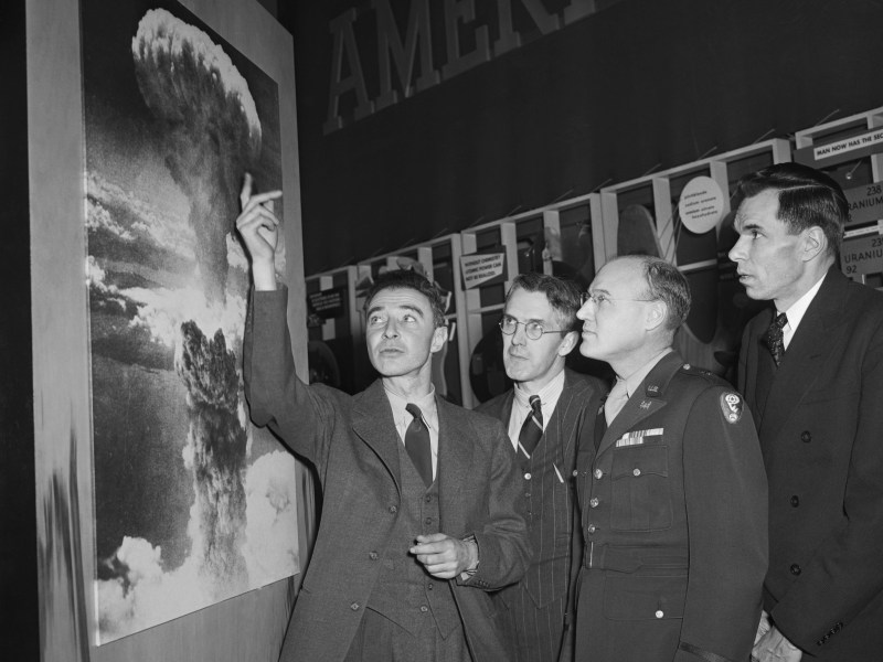 J. Robert Oppenheimer, who was in charge of the Los Alamos, New Mexico, atomic bomb experiment, points to a photograph of the huge column of smoke and flame caused by the actual use of the bomb on Hiroshima, Japan. (Getty Images)