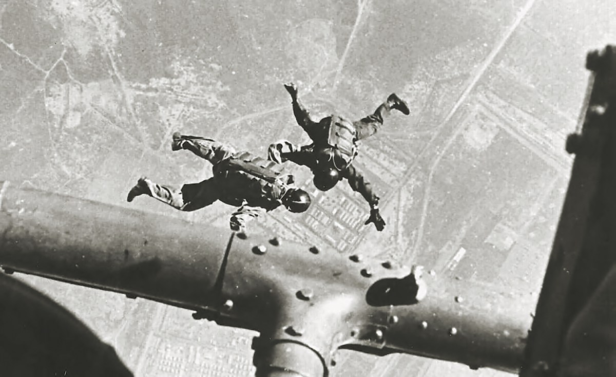 Photo of HALO parachutists of SOG link up beneath a Huey helicopter above Camp Long Thanh.