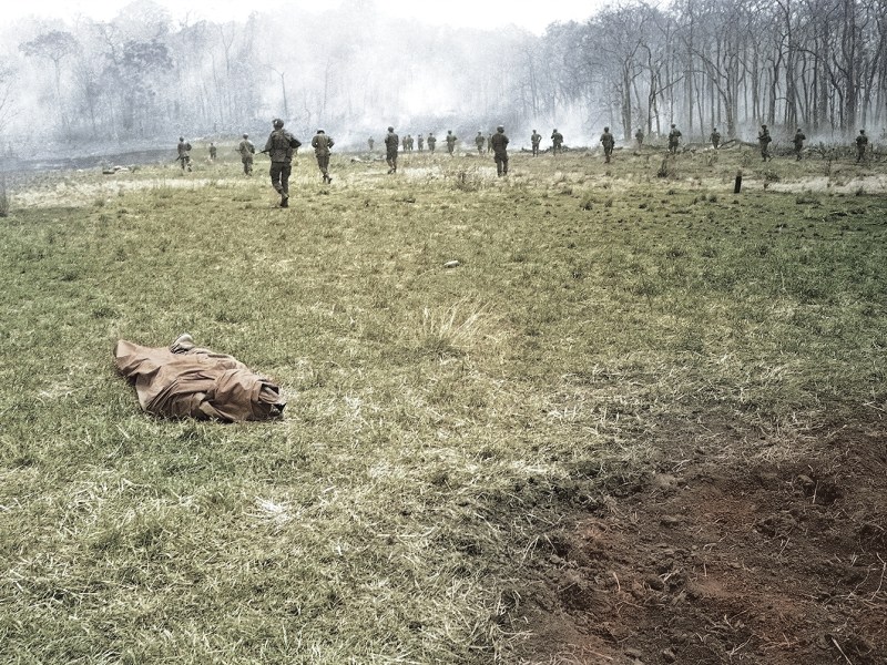 Photo of Infantrymen of the U.S. 4th Division move across clearing passing poncho-wrapped body of a buddy at the spot where he fell in Vietnam on March 23, 1967. Action took place 20 miles northwest of Pleiku in the central highlands of Vietnam, near the Cambodian border.