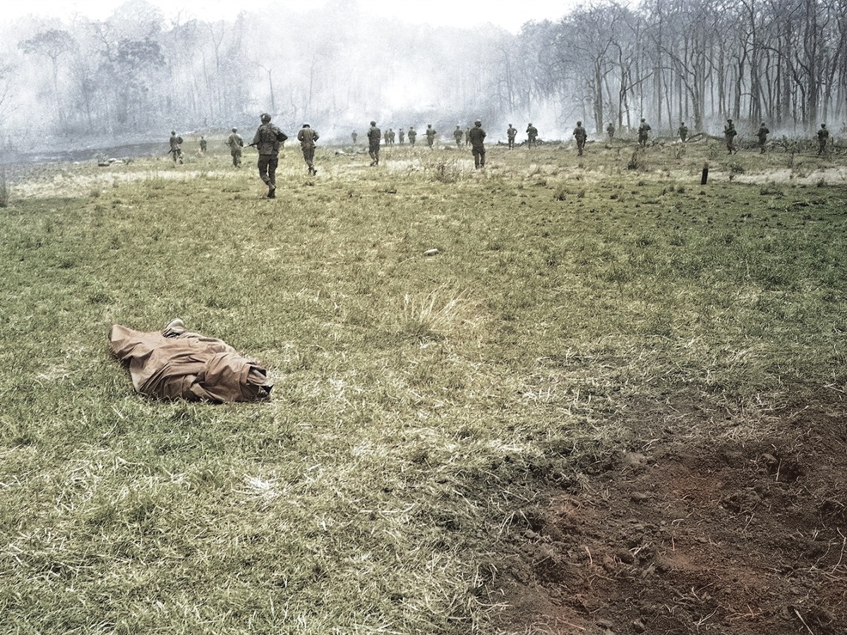 Photo of Infantrymen of the U.S. 4th Division move across clearing passing poncho-wrapped body of a buddy at the spot where he fell in Vietnam on March 23, 1967. Action took place 20 miles northwest of Pleiku in the central highlands of Vietnam, near the Cambodian border.