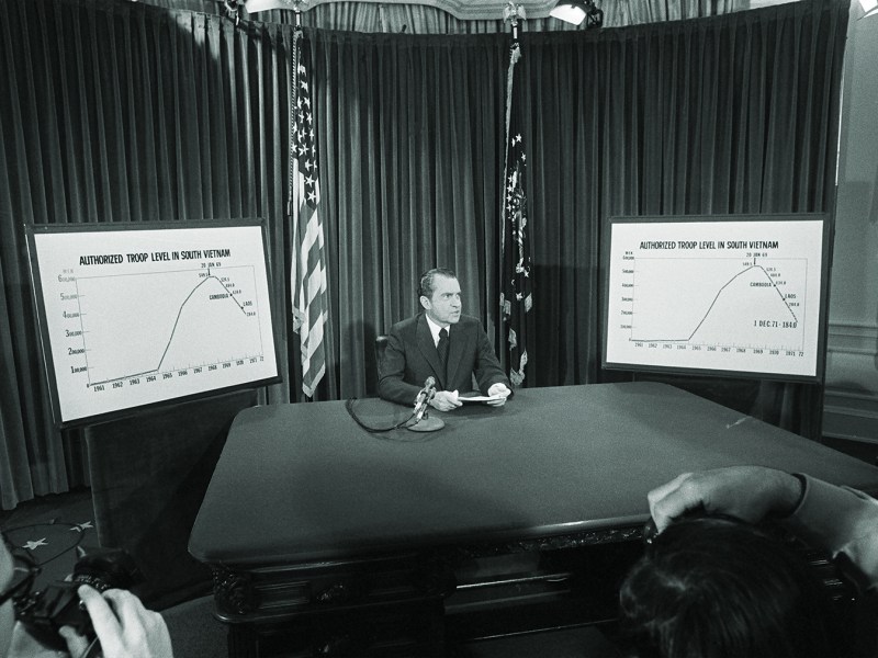 Photo of President Nixon flanked by charts he used to illustrate his televised speech from the White House 4/7 in which he announced he will withdraw an additional 100,000 U.S. troops by December 1. The charts show the authorized troops level in South Vietnam.