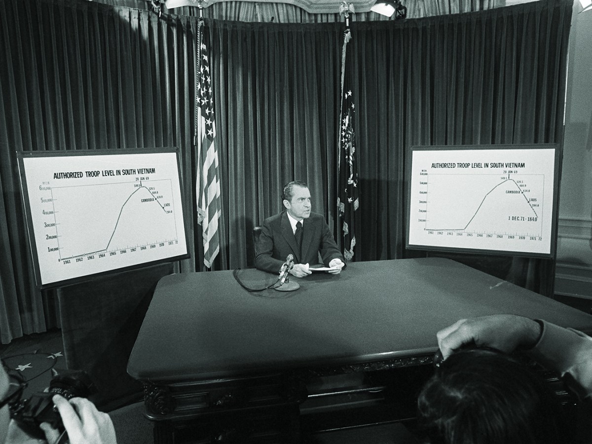Photo of President Nixon flanked by charts he used to illustrate his televised speech from the White House 4/7 in which he announced he will withdraw an additional 100,000 U.S. troops by December 1. The charts show the authorized troops level in South Vietnam.