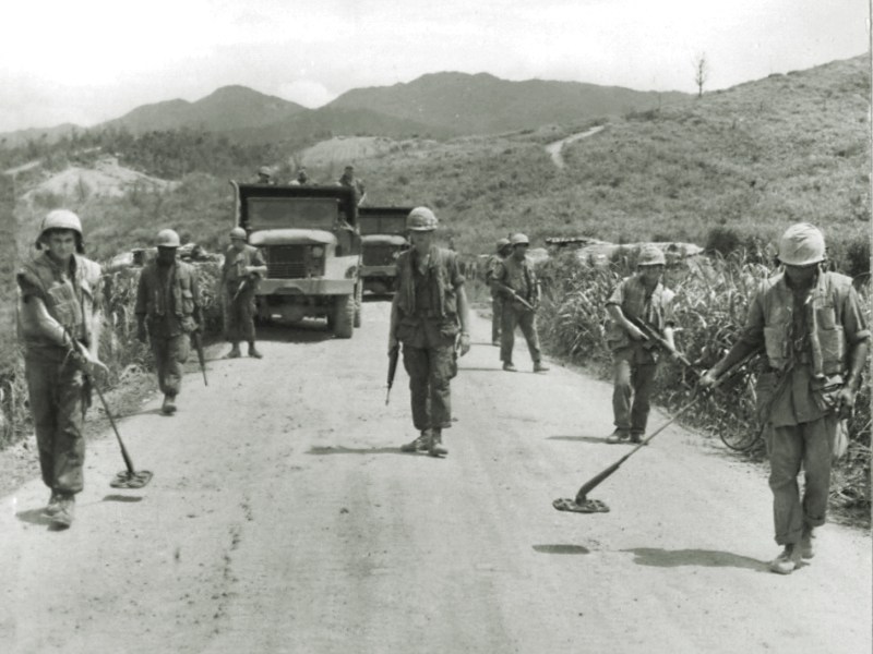 Photo of a Marine mine sweep team checks a road west of Ca Lu for enemy mines in 1968, a duty performed every morning.